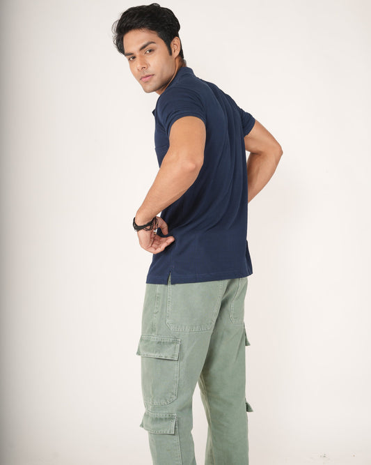 Man wearing a navy blue sleeveless shirt and light green cargo pants on a white background