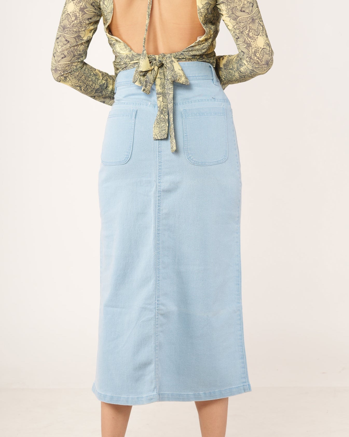 A woman modeling a light blue denim midi skirt with a front button closure.
