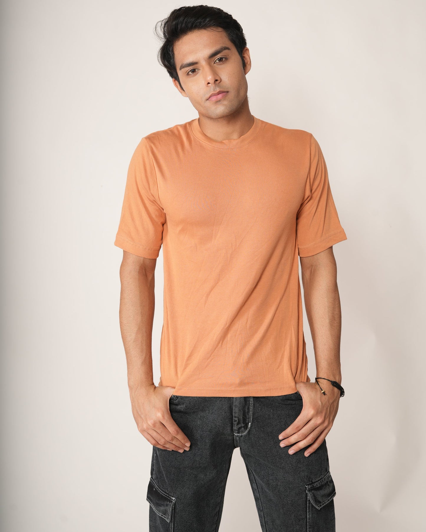Man wearing an peach/orange t-shirt and black pants against a plain background