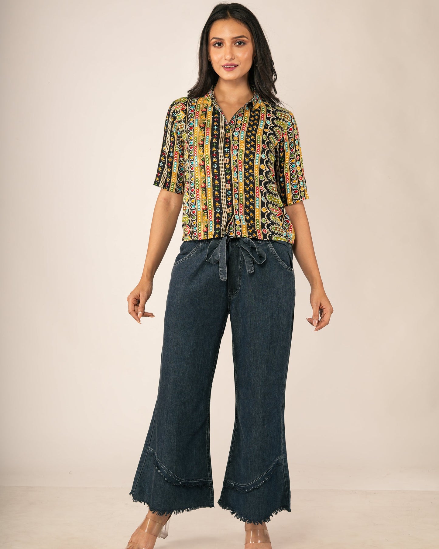 A woman modeling a short-sleeve button-up blouse with a multicolor geometric pattern and dark blue wide-leg jeans,