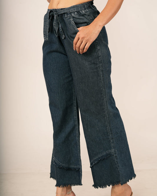 A model wearing dark blue wide-leg cropped jeans with a drawstring waistband and frayed hems, paired with a patterned crop top.