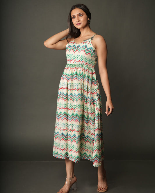 A woman modeling a sleeveless midi dress with a colorful geometric zigzag pattern in green, orange, and white