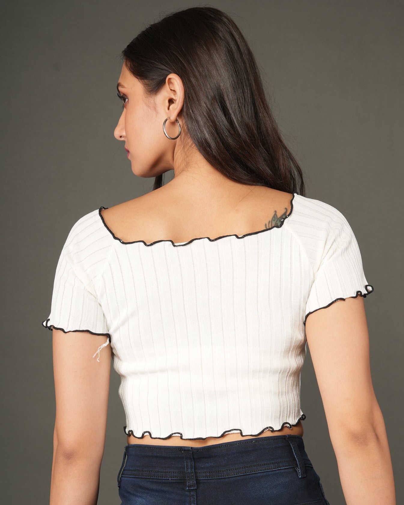 A woman modeling a white off-the-shoulder short-sleeve crop top and dark blue high-waisted wide-leg jeans.