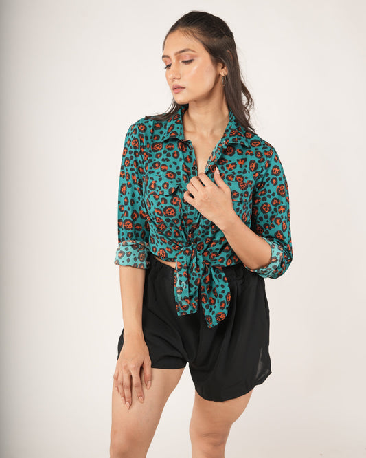 Woman wearing a leopard patterned teal shirt and black shorts on a white background
