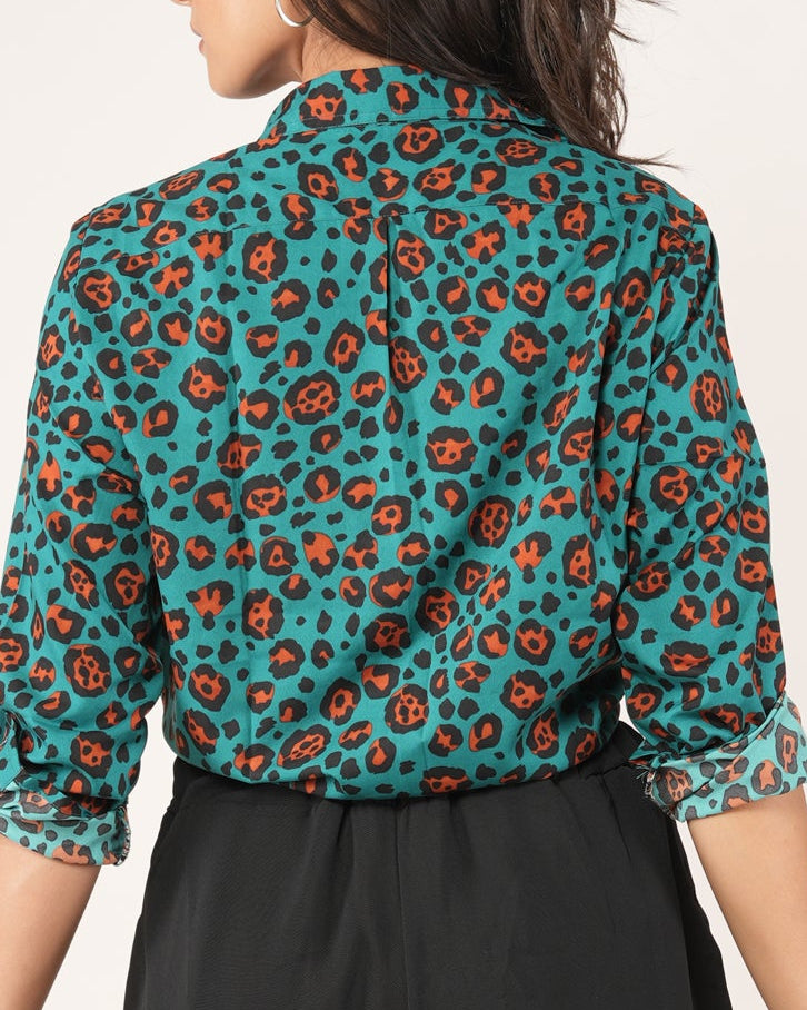 Woman wearing a leopard patterned teal shirt and black shorts on a plain background