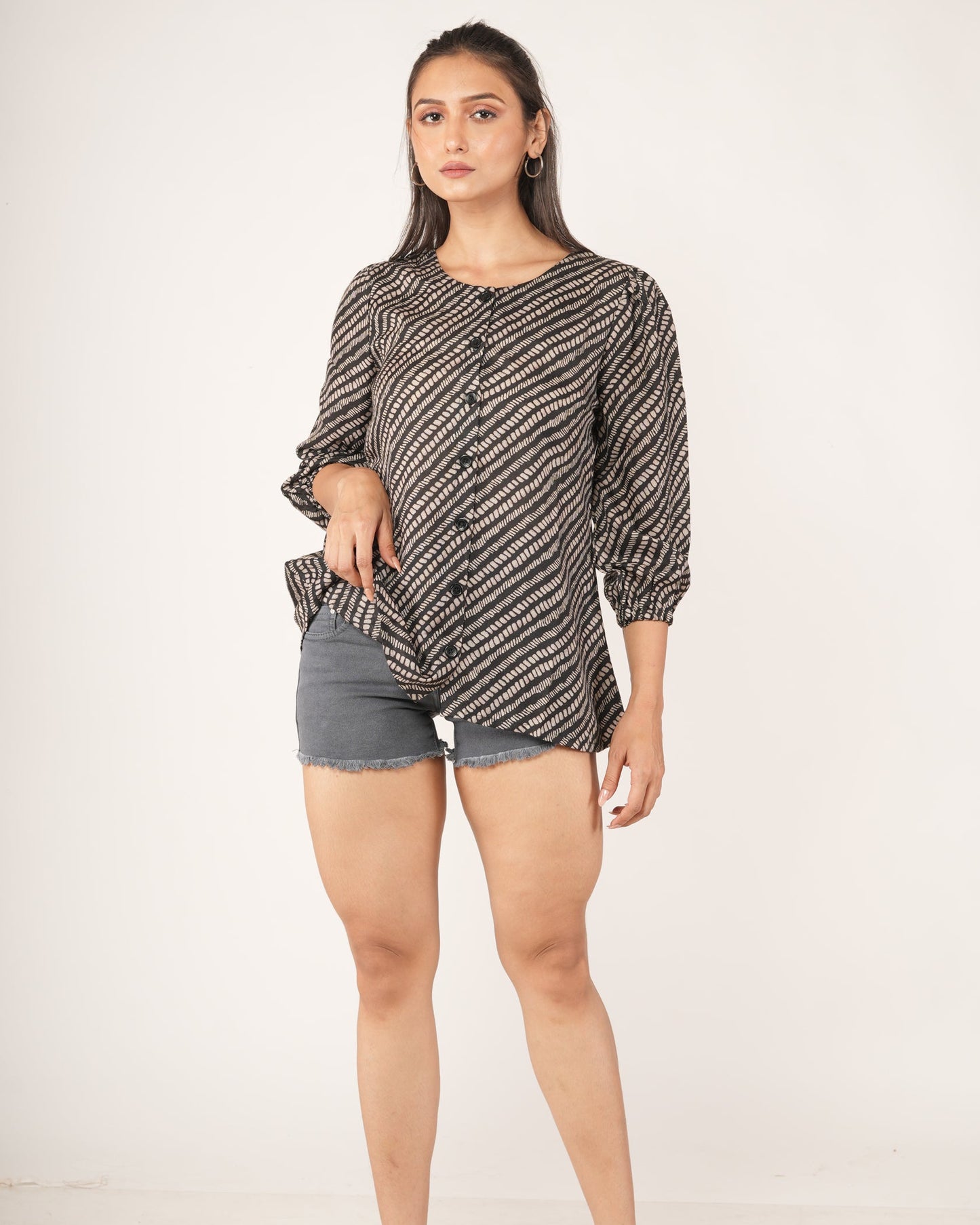 Woman wearing a snake patterned top and gray shorts on a white background