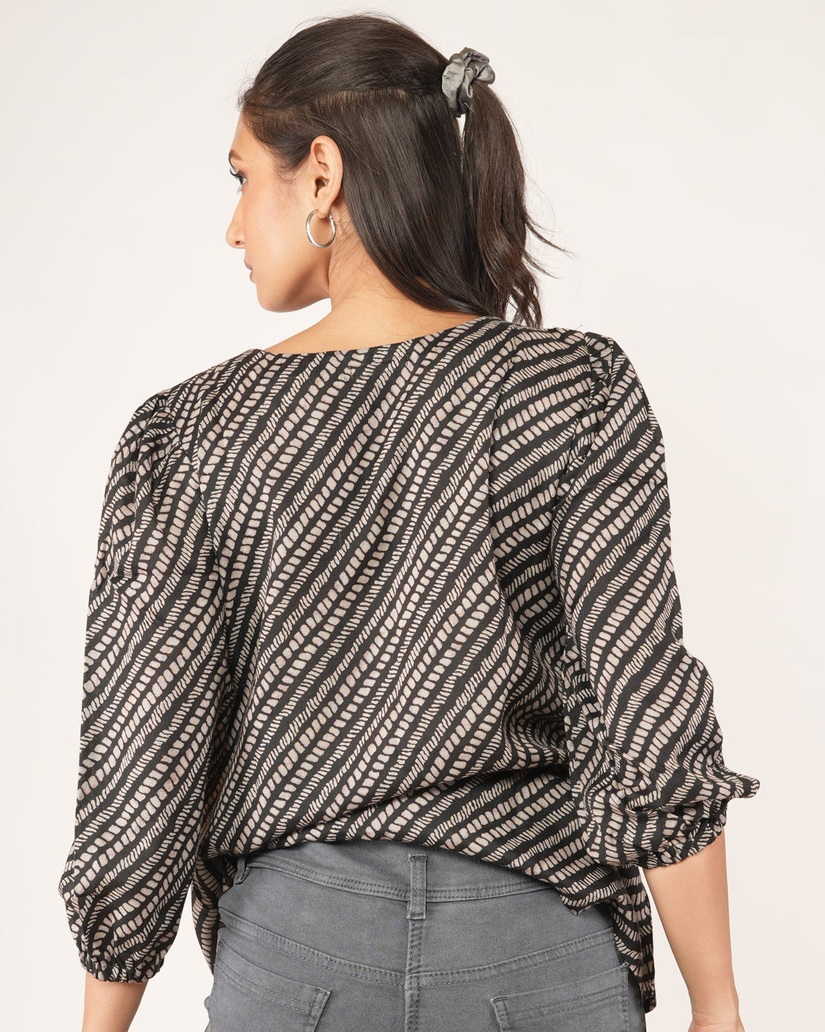 Woman wearing a patterned top and denim shorts on a plain background