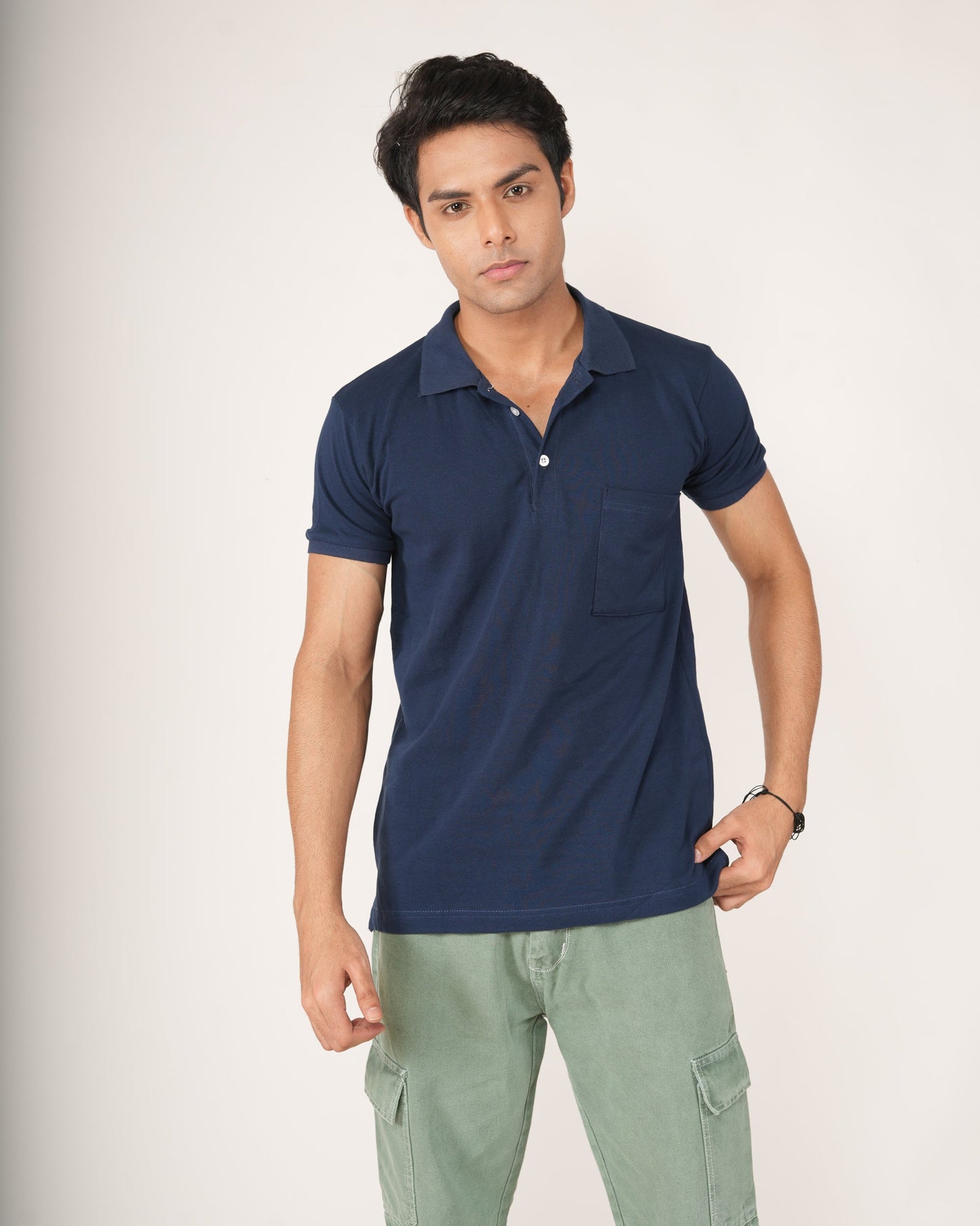 Man wearing a navy blue polo shirt and light green pants on a white background