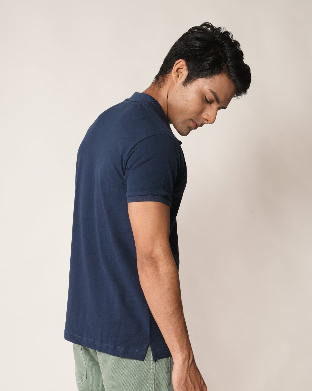 Man wearing a navy blue shirt and light green cargo pants against a plain background