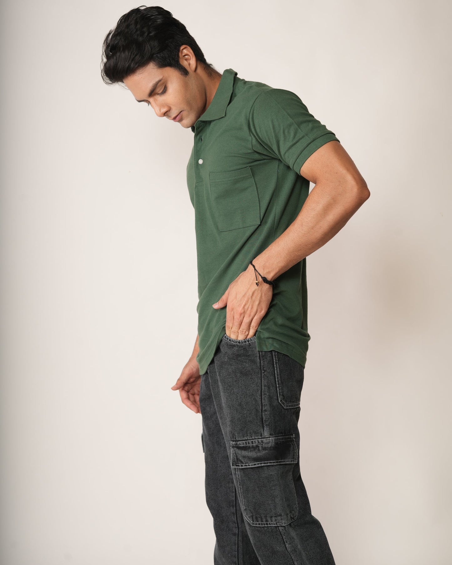 Man wearing a green polo shirt and dark jeans against a plain background