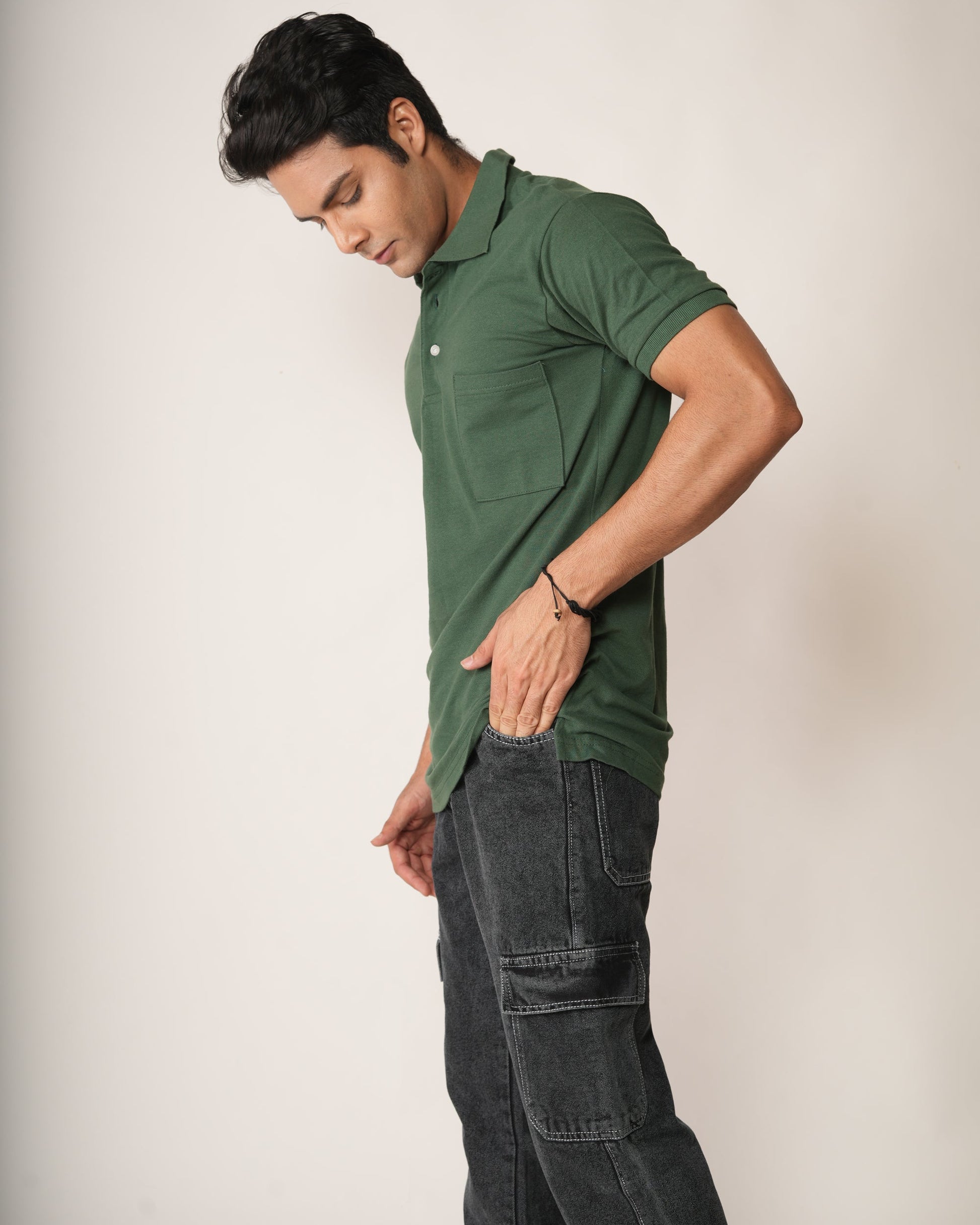 Man wearing a green polo shirt and dark jeans against a plain background