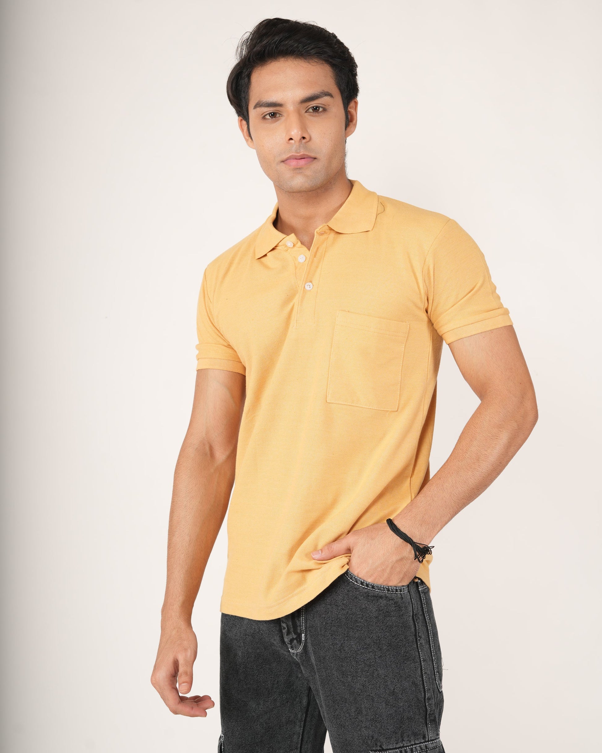 Man wearing a yellow polo shirt and dark jeans against a white background