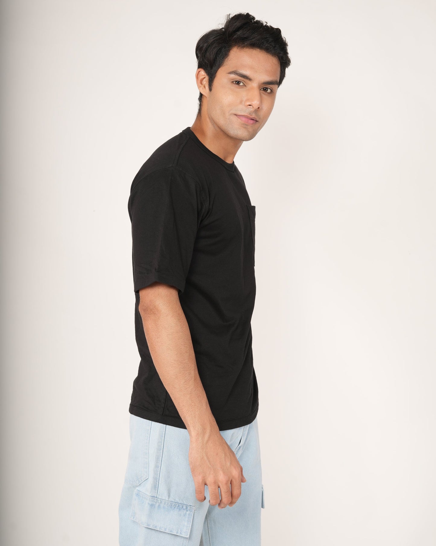 Man wearing a black t-shirt and light blue pants on a white background