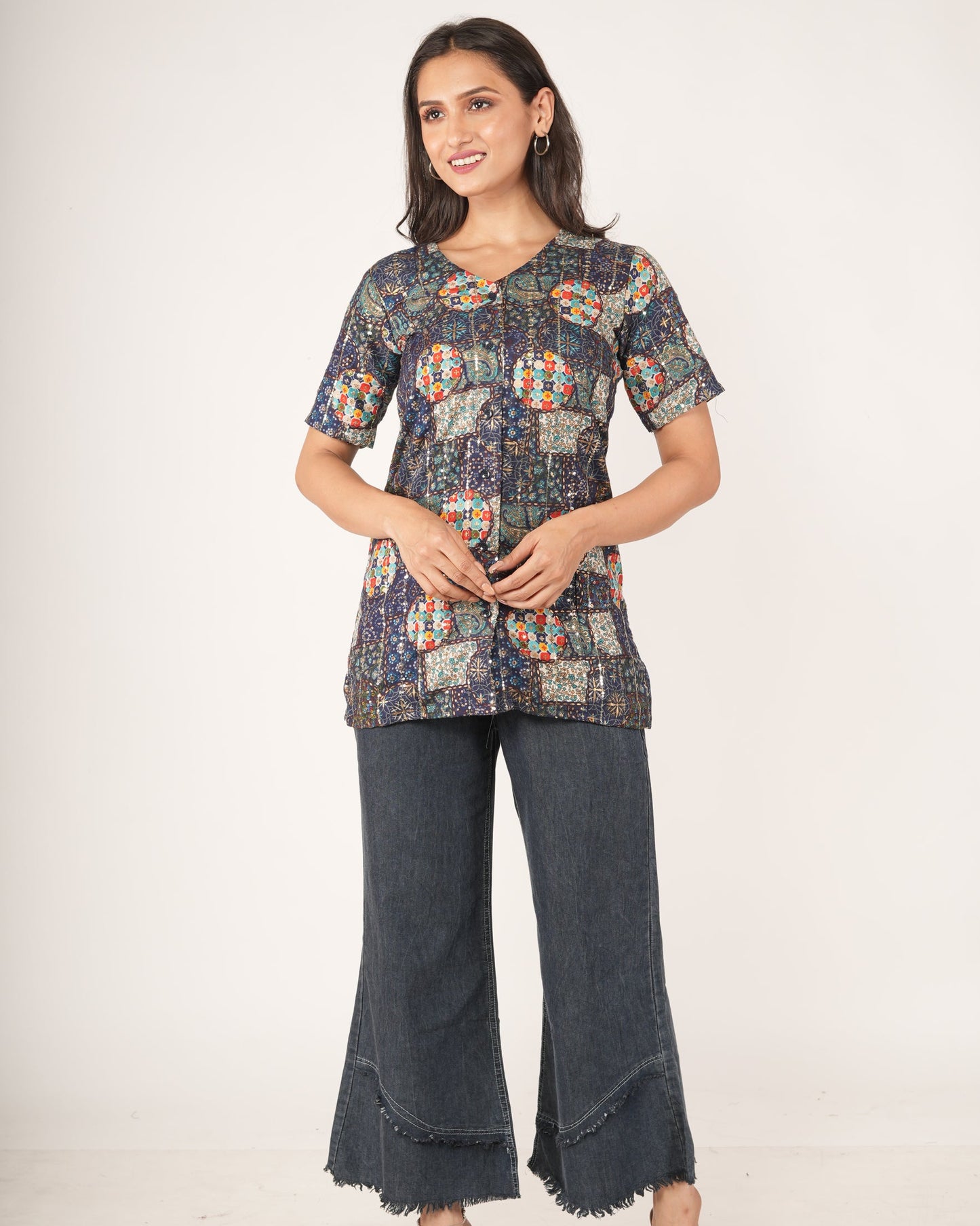 A woman modeling a short-sleeveEthnic Fusion Embroidered Sequin Top paired with dark gray wide-leg jeans and beige sandals, against a plain light gray studio background.