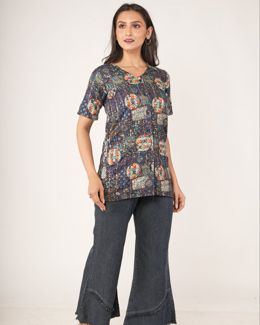A woman modeling a short-sleeve Ethnic Fusion Embroidered Sequin Top , paired with dark gray flared jeans .
