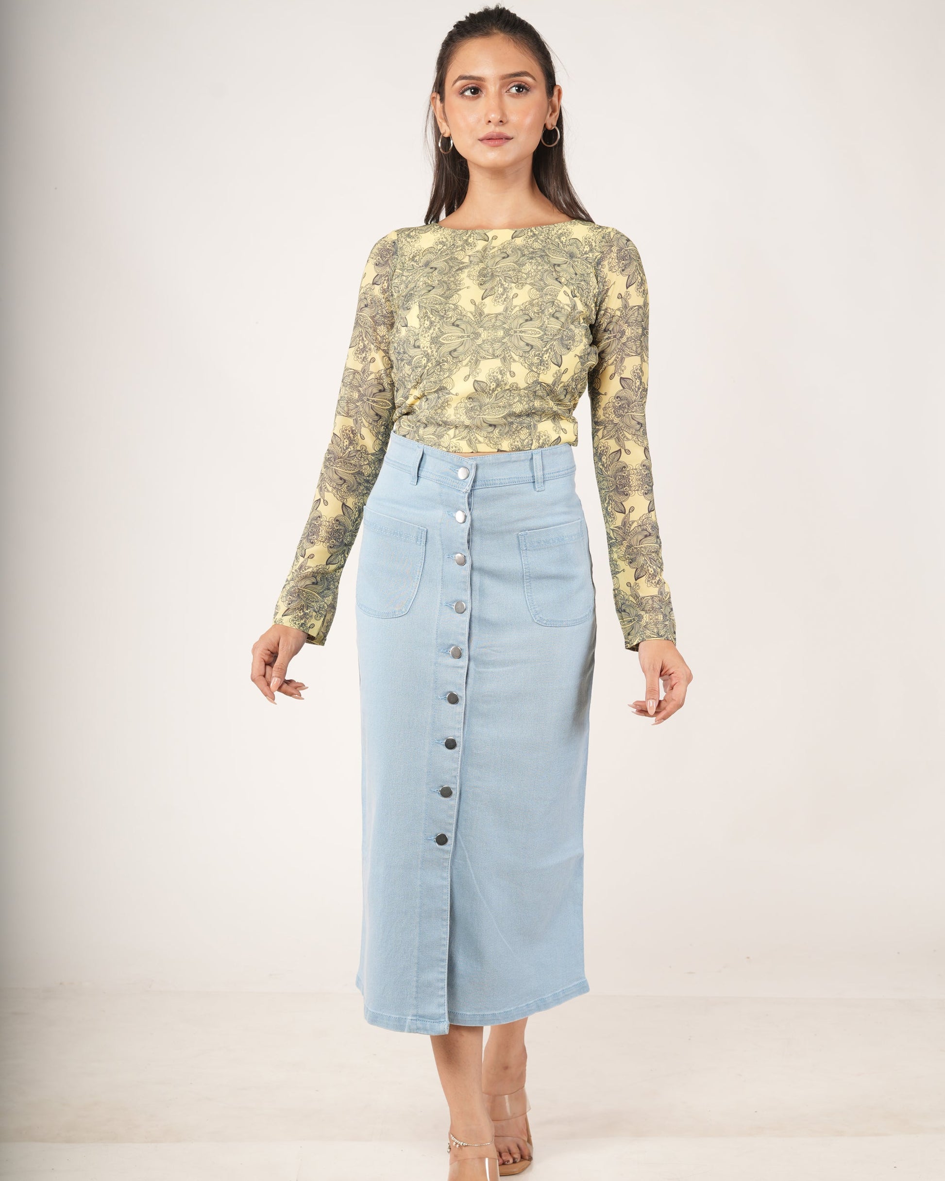 A woman modeling a light blue denim midi skirt with a front button closure.