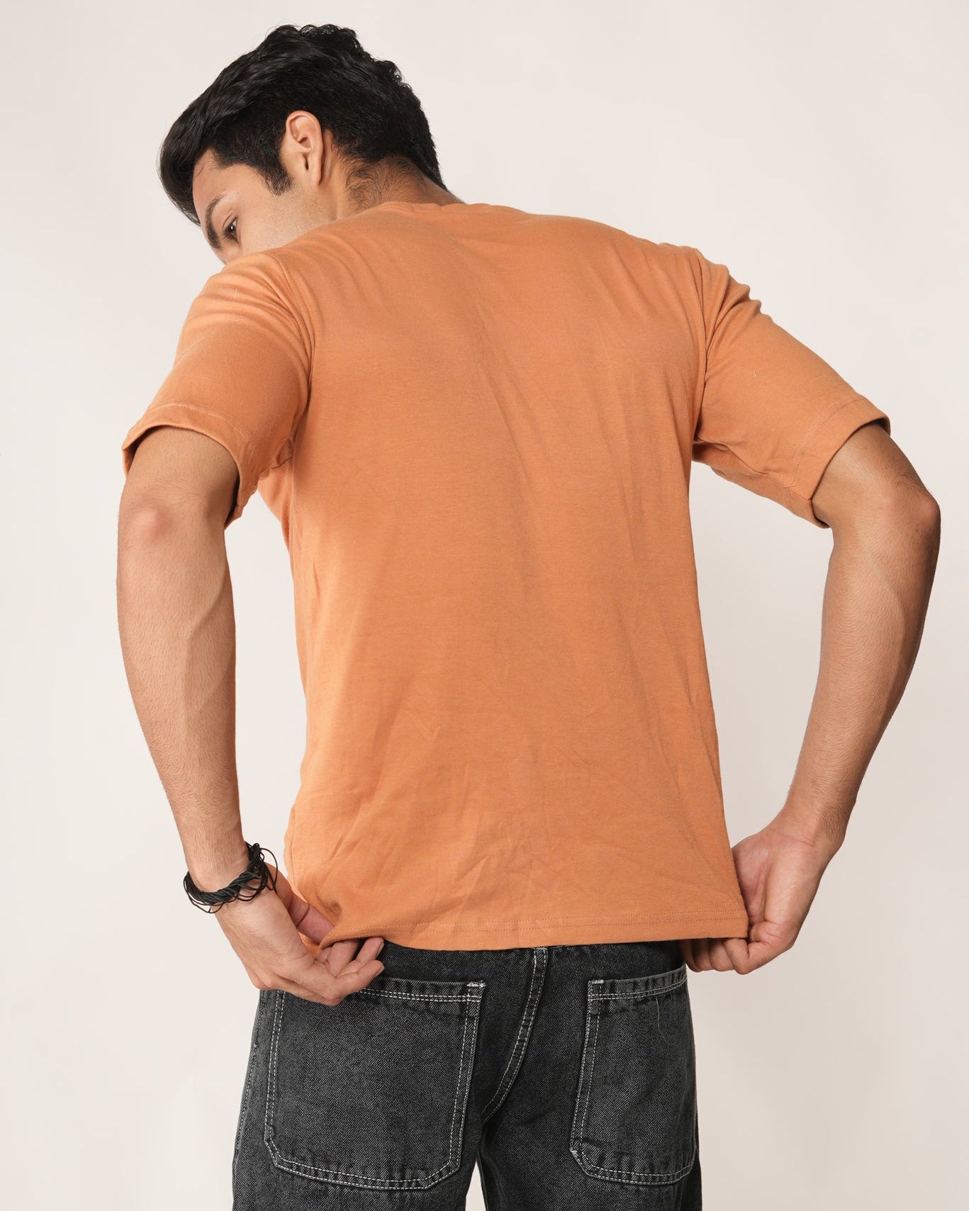 Person wearing an peach/orange t-shirt and dark jeans against a plain background