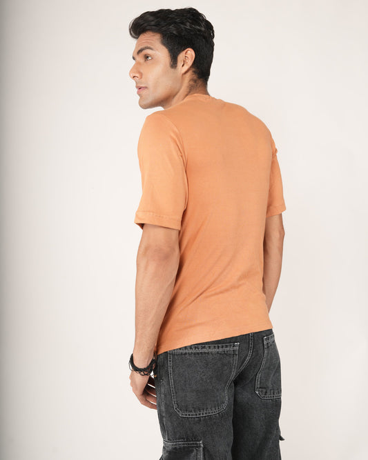 Man wearing an peach/orange t-shirt and black pants against a white background