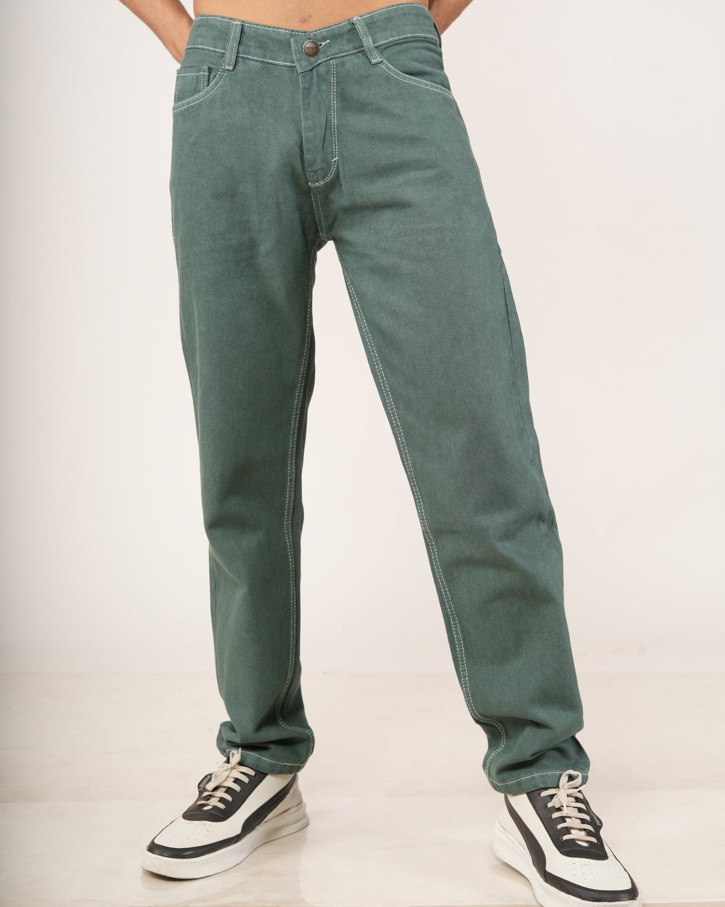 A person modeling a pair of relaxed-fit green jeans with hands in pockets, paired with black and white sneakers.