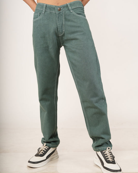 A person modeling a pair of relaxed-fit green jeans with hands in pockets, paired with black and white sneakers.