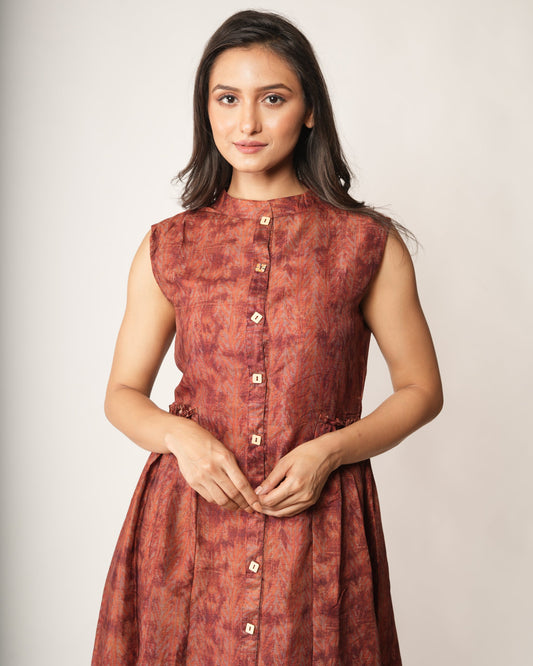 Woman wearing a rust-colored sleeveless dress against a plain background