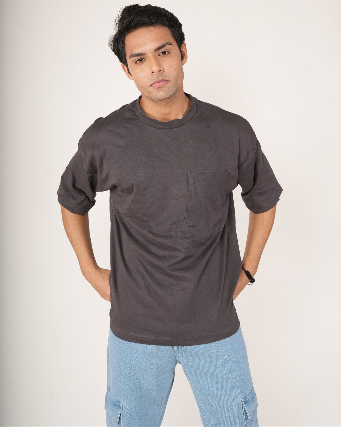 Man wearing a slate gray t-shirt with a pocket and light blue jeans.