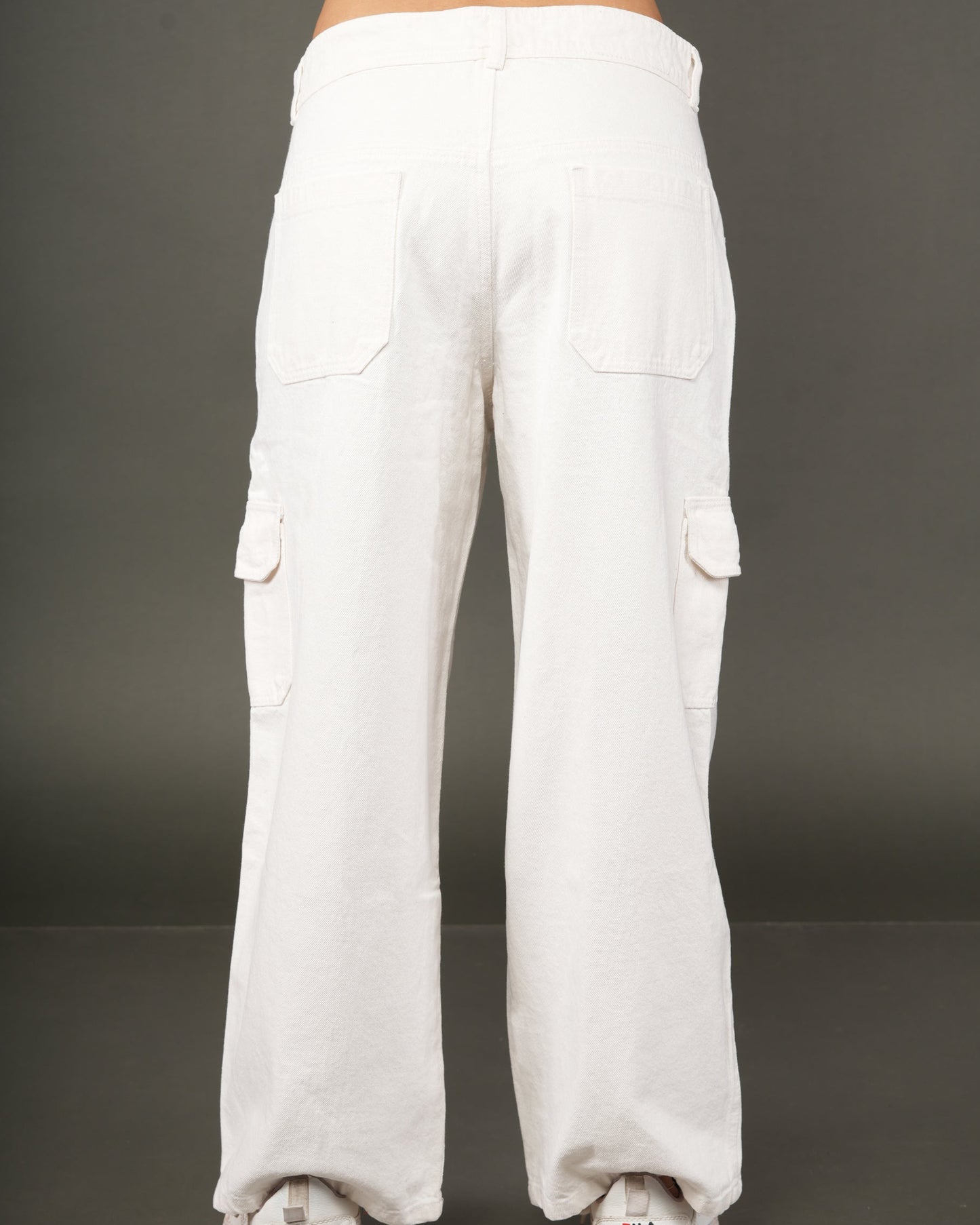 White wide-leg cargo pants shown from the back on a model, featuring large back pockets and side flap pockets, paired with white sneakers.