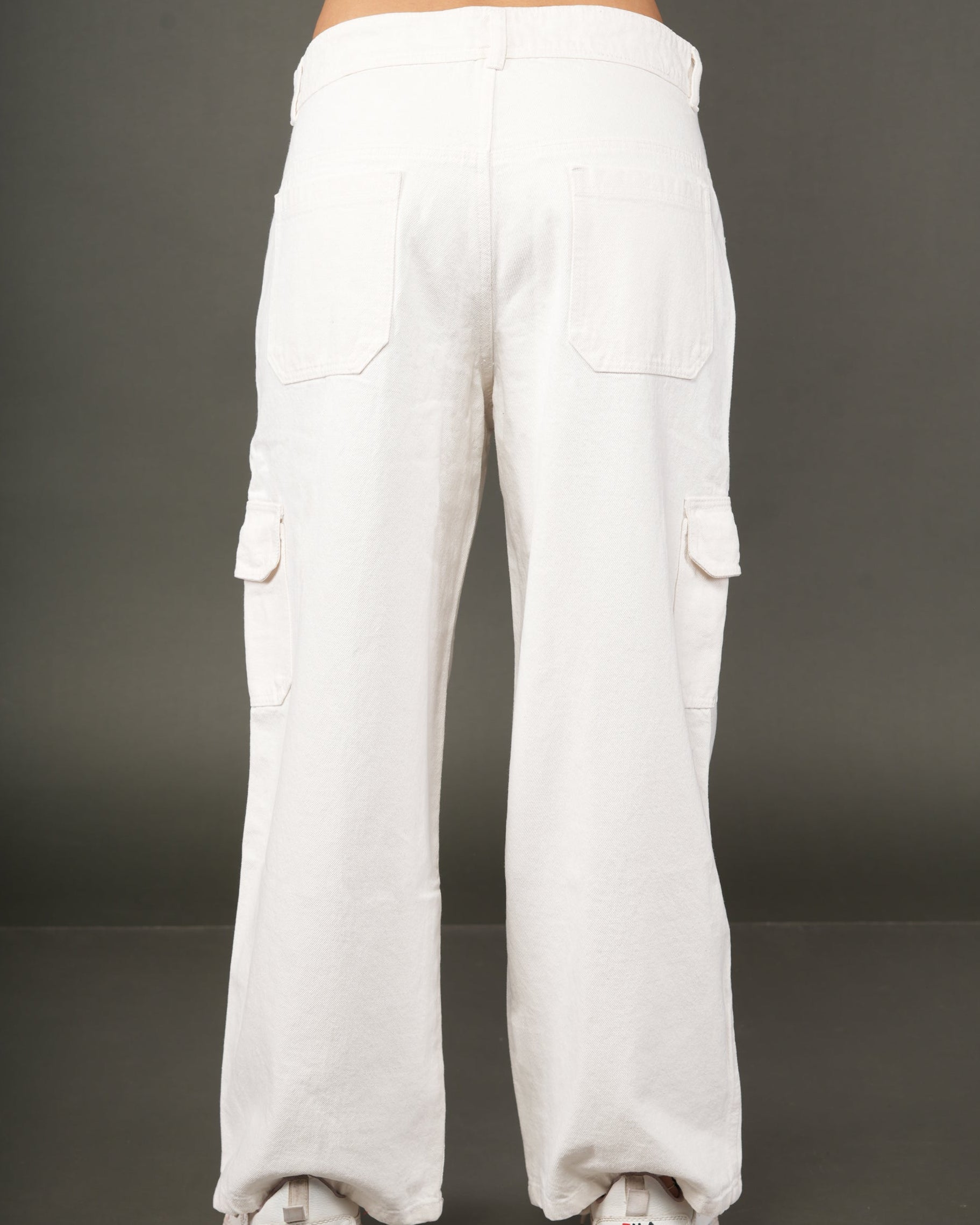 White wide-leg cargo pants shown from the back on a model, featuring large back pockets and side flap pockets, paired with white sneakers.