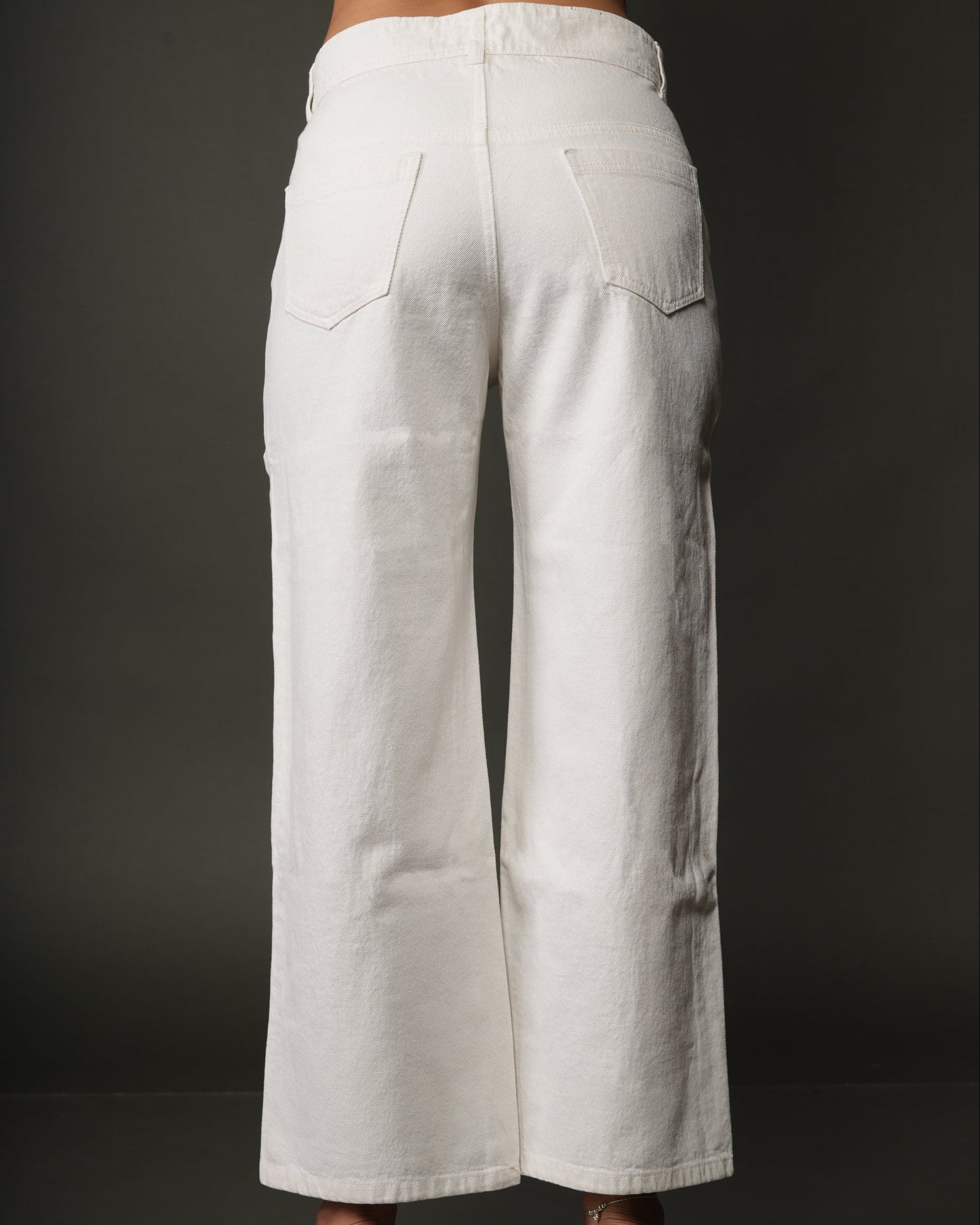 White wide-leg cropped pants shown from the back on a model, featuring a straight waistband, back pockets, and a relaxed leg fit, paired with clear block-heel sandals.