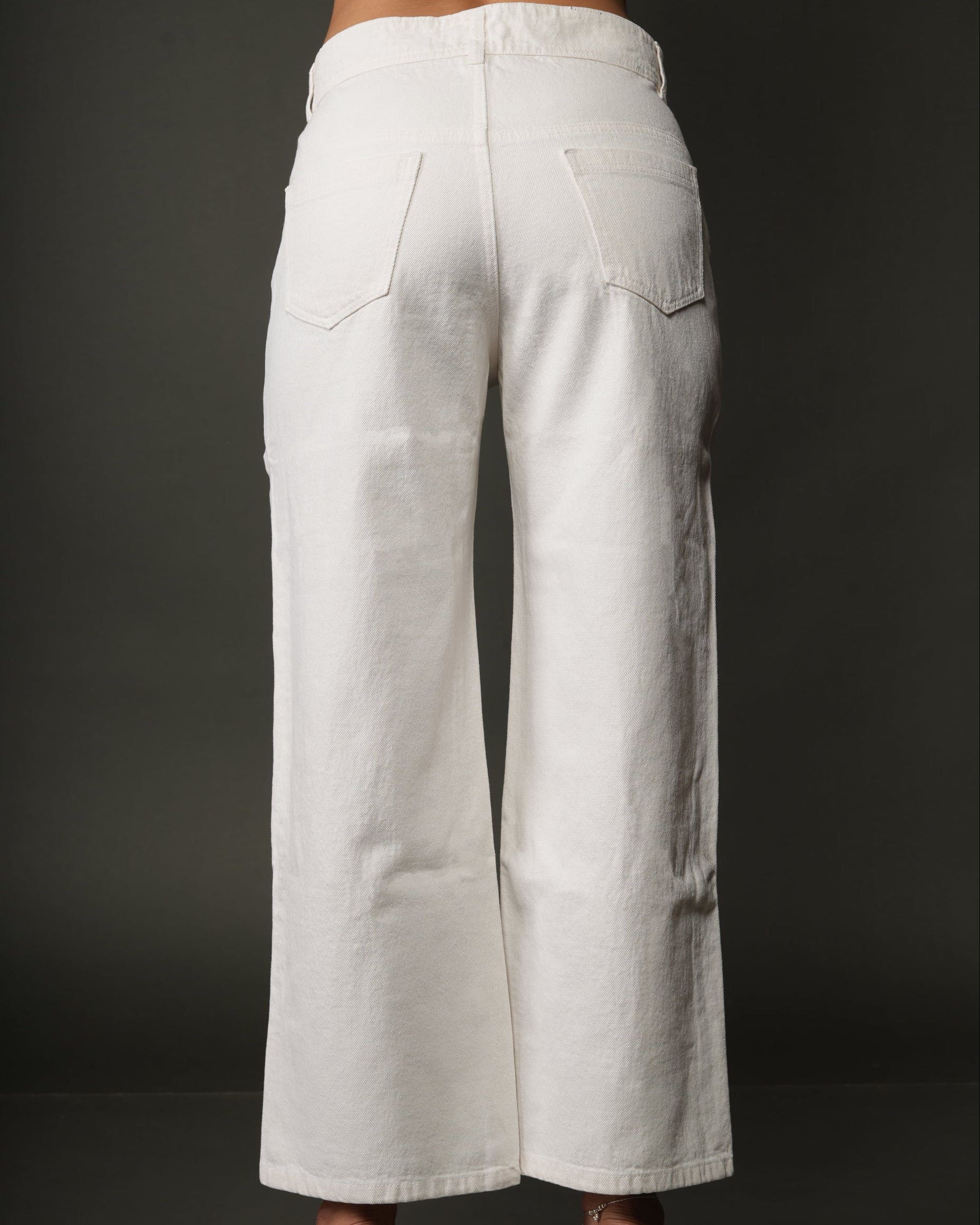 White wide-leg cropped pants shown from the back on a model, featuring a straight waistband, back pockets, and a relaxed leg fit, paired with clear block-heel sandals.