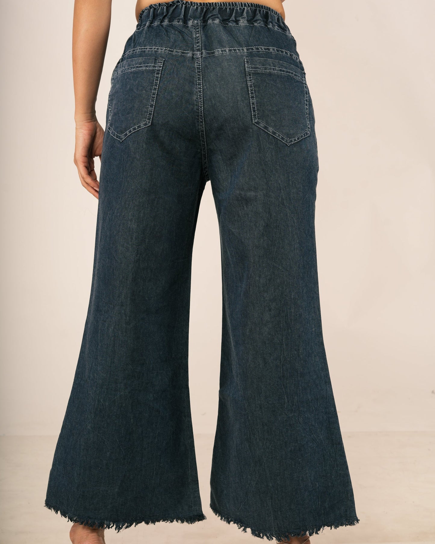 Back view of a model wearing dark blue wide-leg denim jeans with a frayed hem, paired with a patterned short-sleeve crop top.