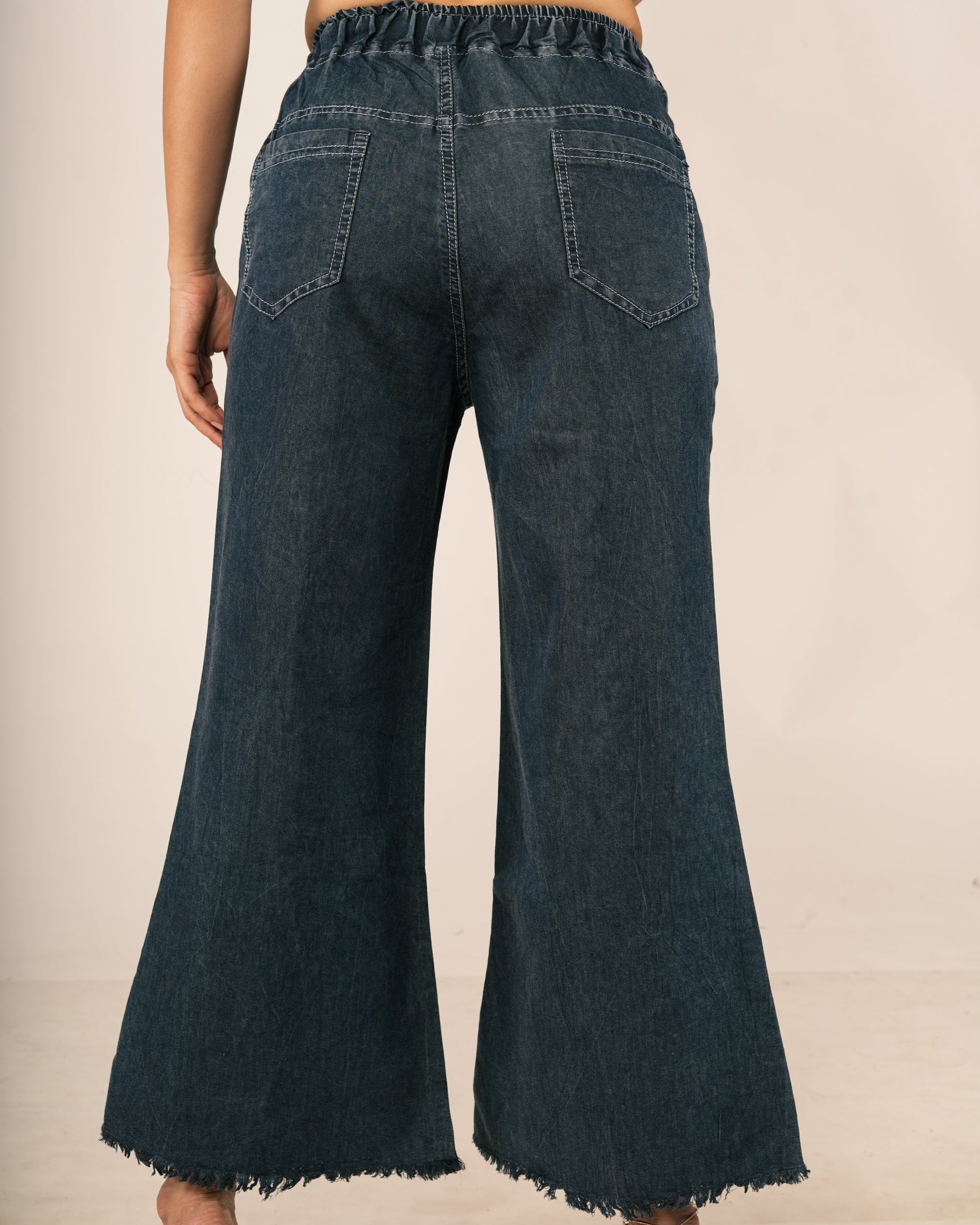 Back view of a model wearing dark blue wide-leg denim jeans with a frayed hem, paired with a patterned short-sleeve crop top.