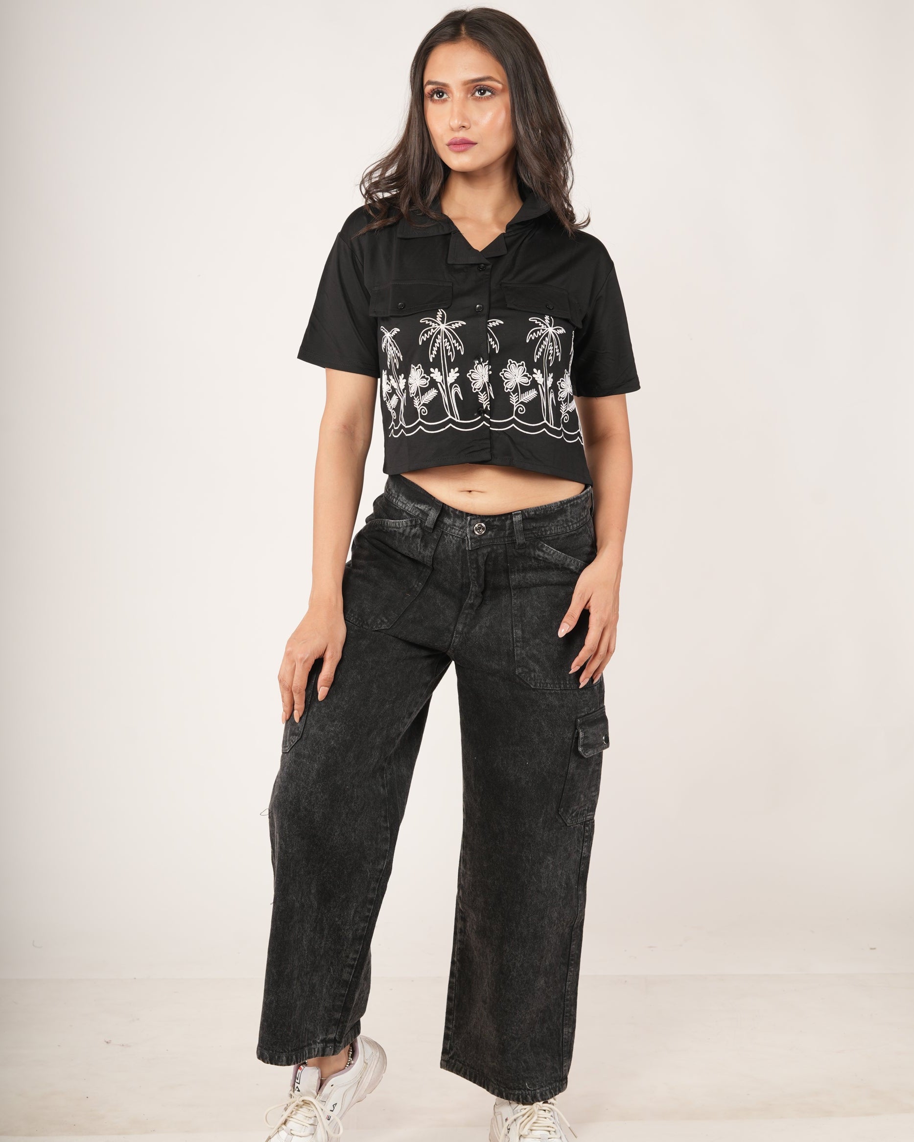 Woman wearing a black crop top with palm tree design and black jeans.