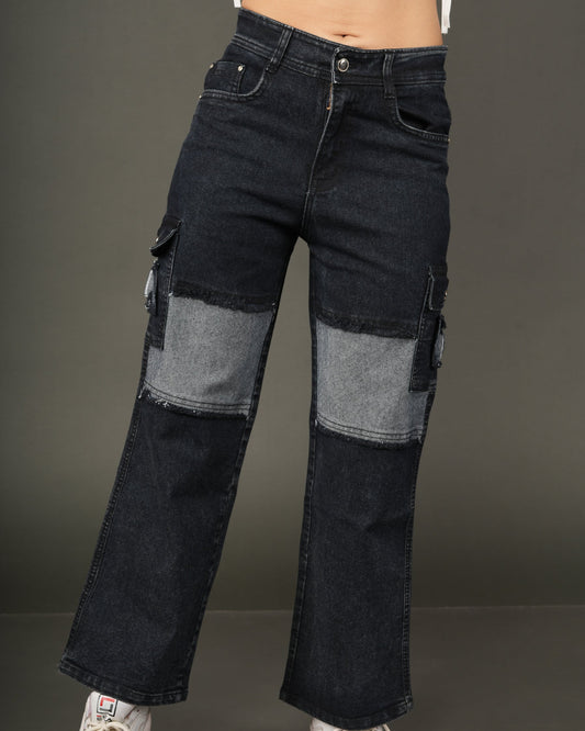 A person wearing dark blue patchwork cargo flare jeans with lighter blue denim panels on the thighs, styled with a white cropped tie-front top and white sneakers.