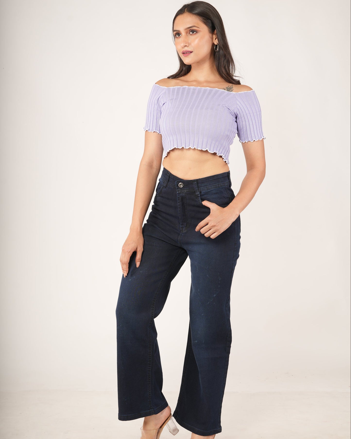 A woman modeling a light purple ribbed off-the-shoulder crop top and dark navy wide-leg jeans.