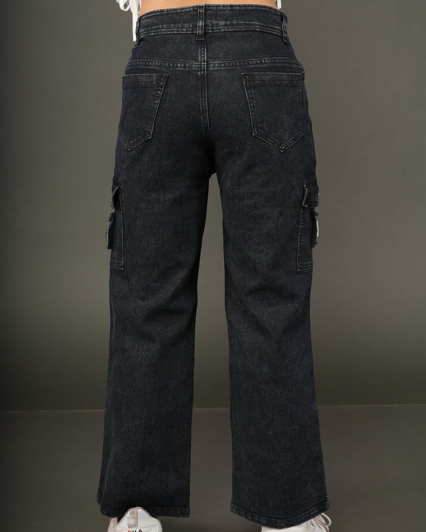 Rear view of a person wearing dark washed wide-leg cargo jeans, a white cropped top, and white sneakers.