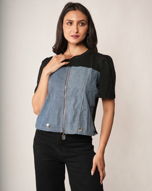 A woman modeling a short-sleeve color-blocked top with a denim blue front panel, black sleeves and side panels, and a front zipper.