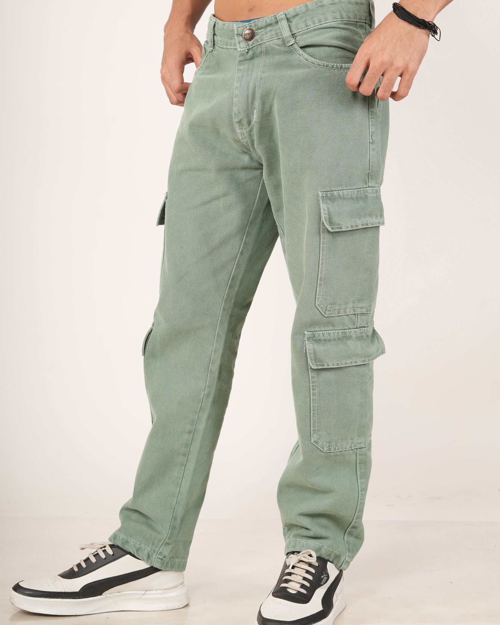A man wearing sage green 8 pocket cargo jeans with side flap pockets and black-and-white sneakers.