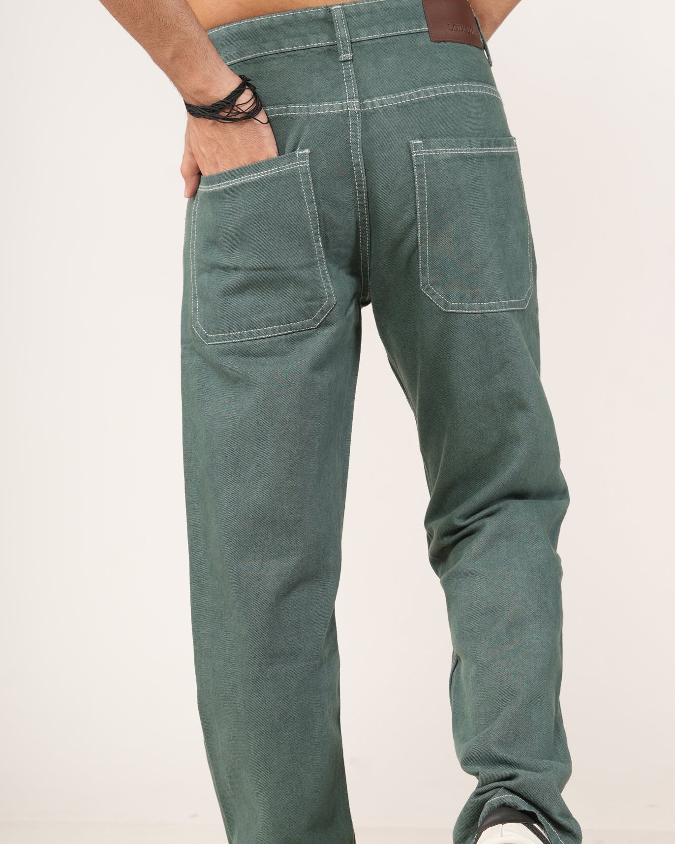 A man wearing green denim jeans, shown from the back as he walks, with his hands in his pockets.