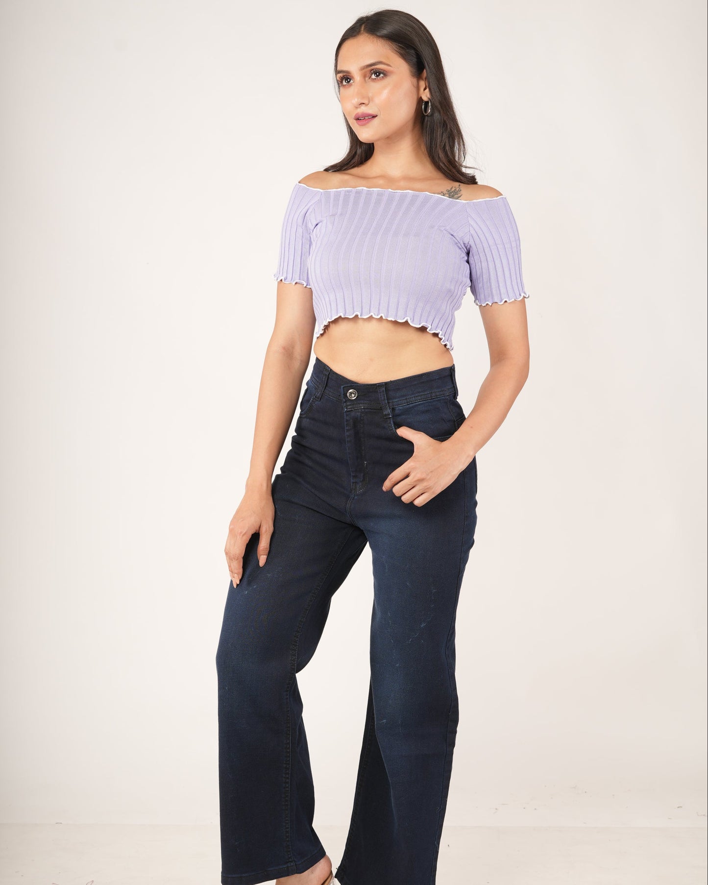 A woman modeling a lavender/light purple off-the-shoulder ribbed crop top  and dark navy wide-leg jeans.