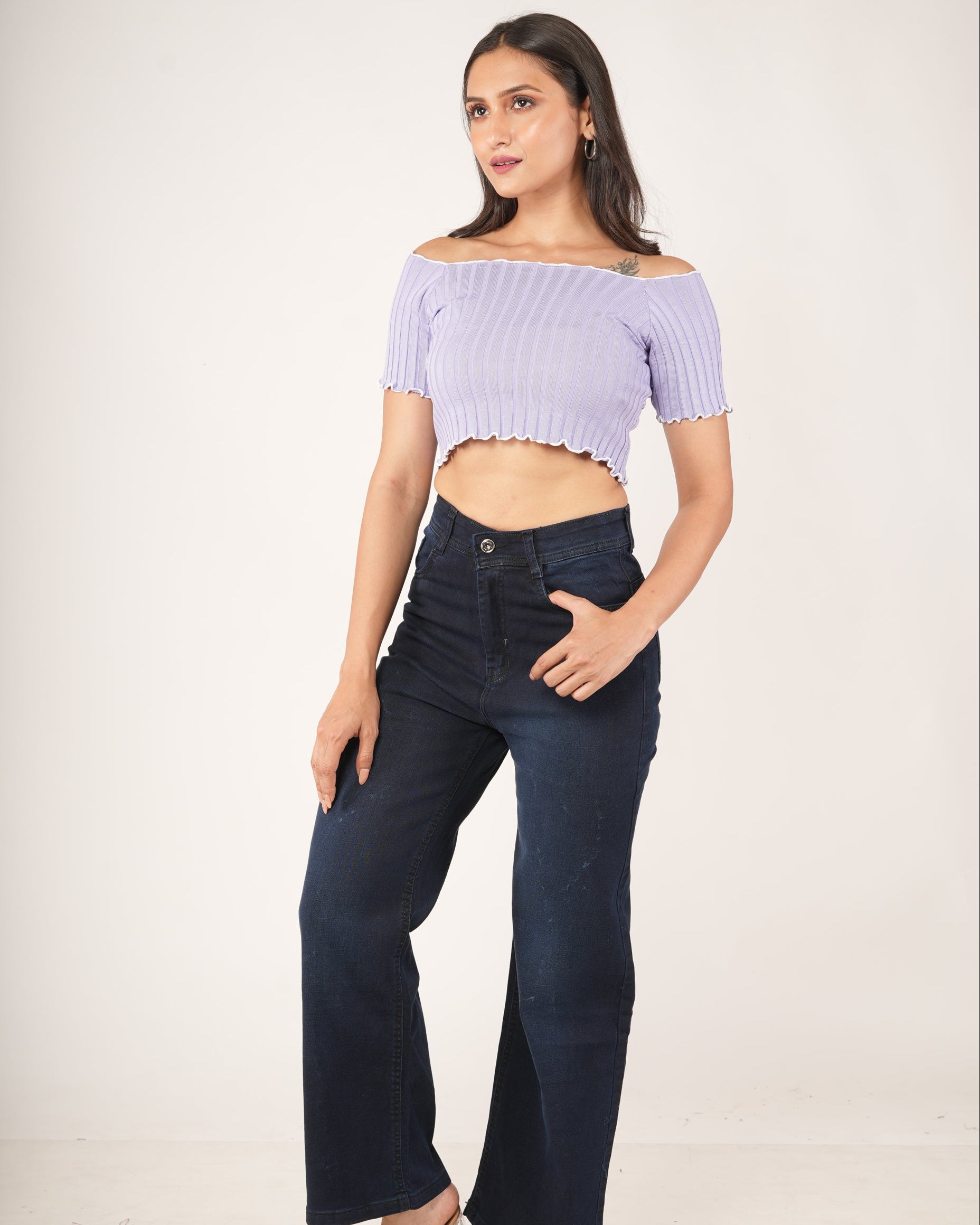A woman modeling a lavender/light purple off-the-shoulder ribbed crop top  and dark navy wide-leg jeans.
