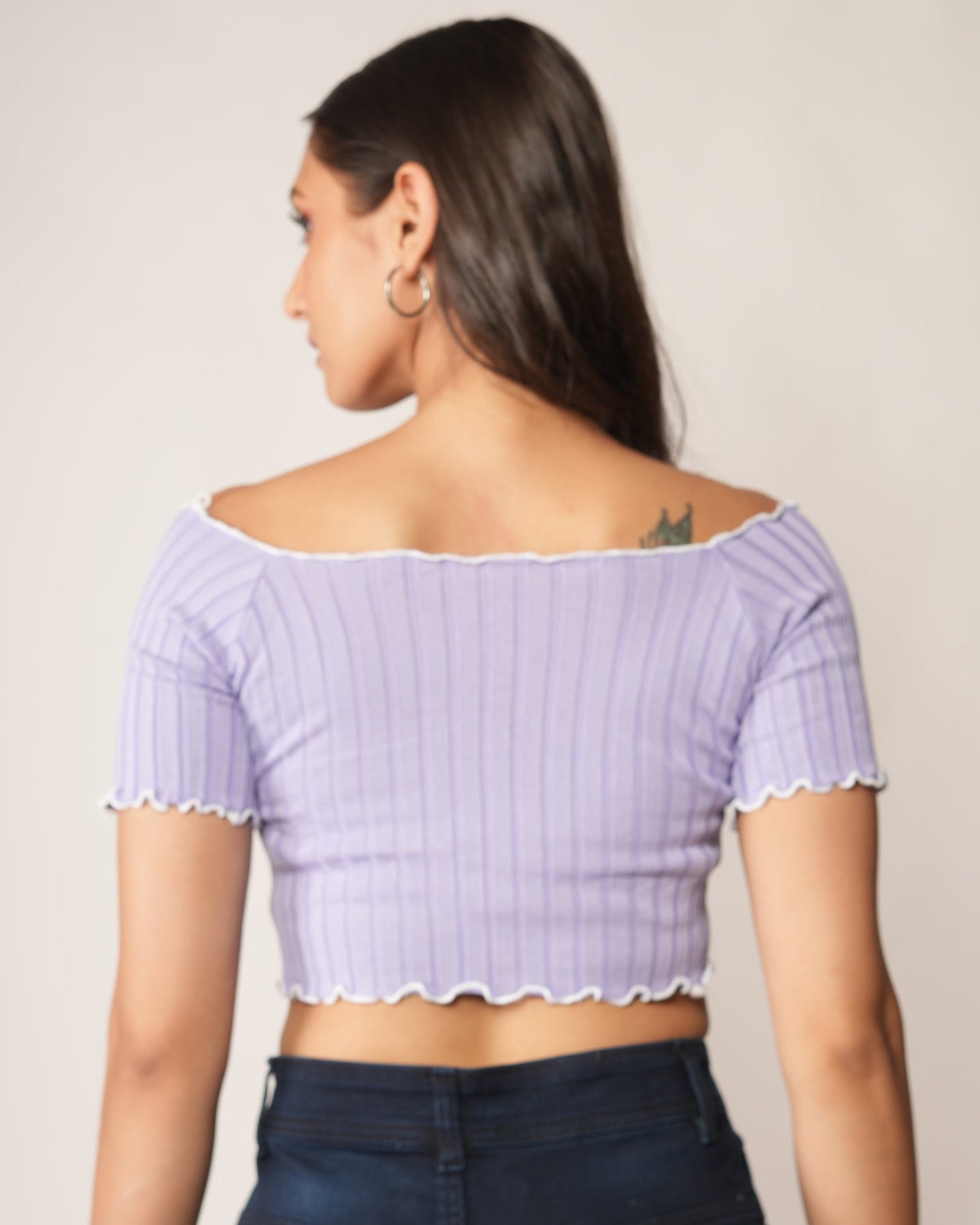 A woman modeling a lavender/light purple off-the-shoulder ribbed crop top  and dark navy wide-leg jeans.
