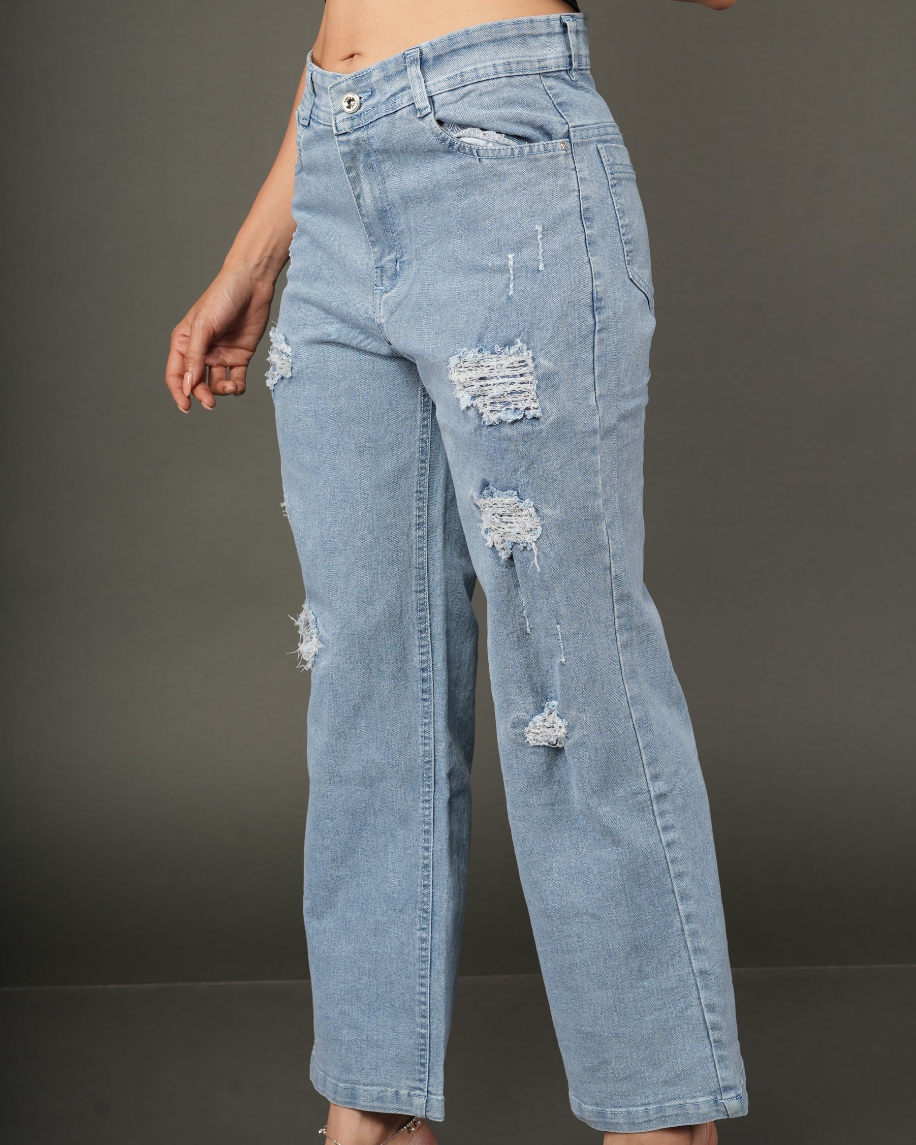 A model wearing light-wash blue distressed jeans with ripped details, paired with a dark navy satin crop top.