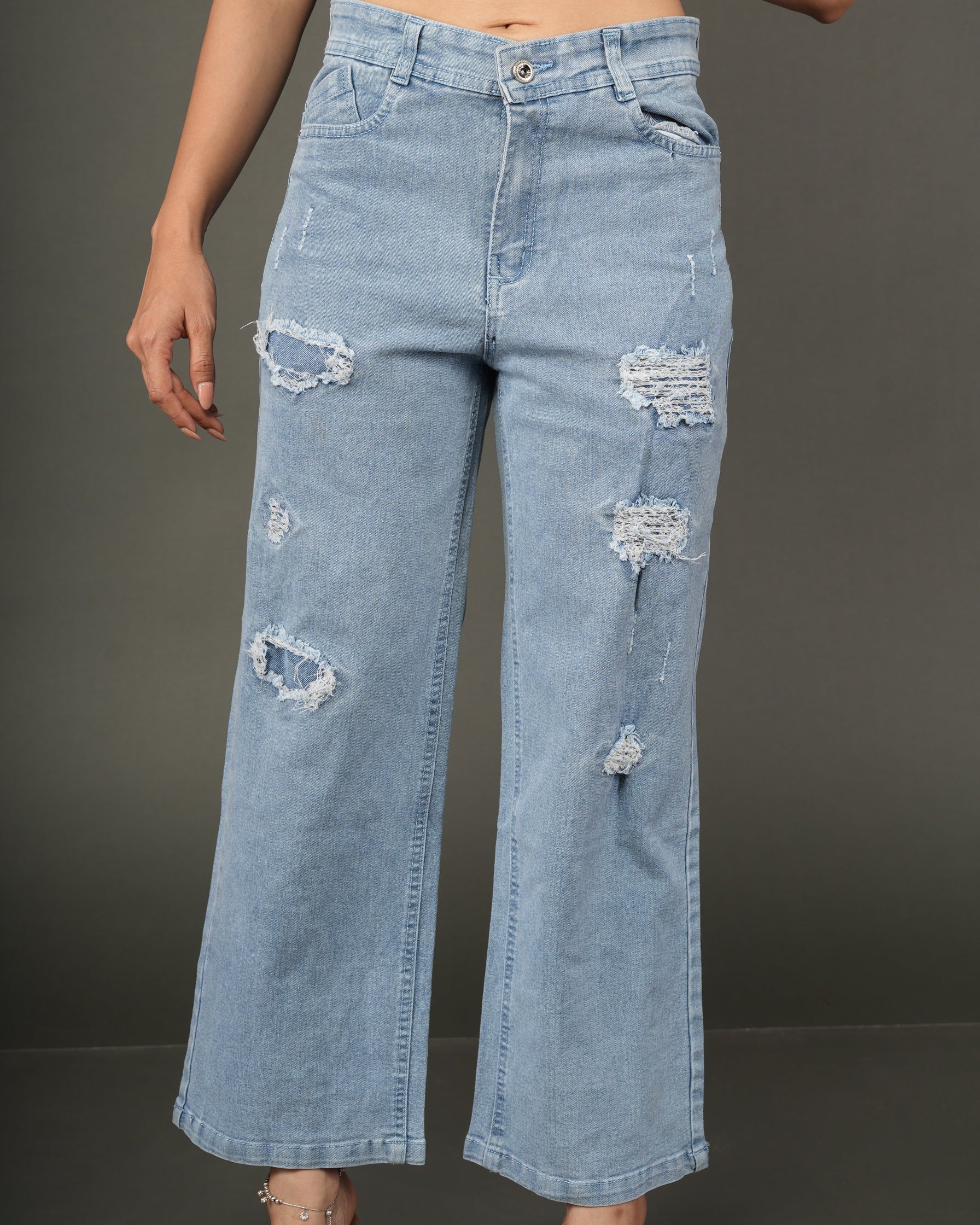 A model wearing light-wash blue distressed wide-leg jeans, paired with a dark navy satin crop top.