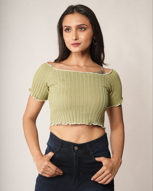 A woman modeling a light olive green ribbed short-sleeve crop top with a ruffled neckline, paired with dark blue jeans.