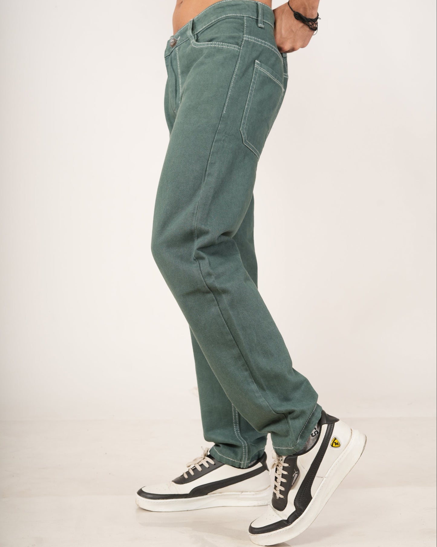 A person modeling a pair of relaxed-fit green jeans with hands in pockets, paired with black and white sneakers.