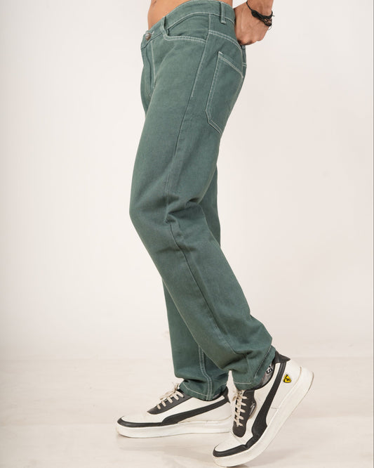 A person modeling a pair of relaxed-fit green jeans with hands in pockets, paired with black and white sneakers.
