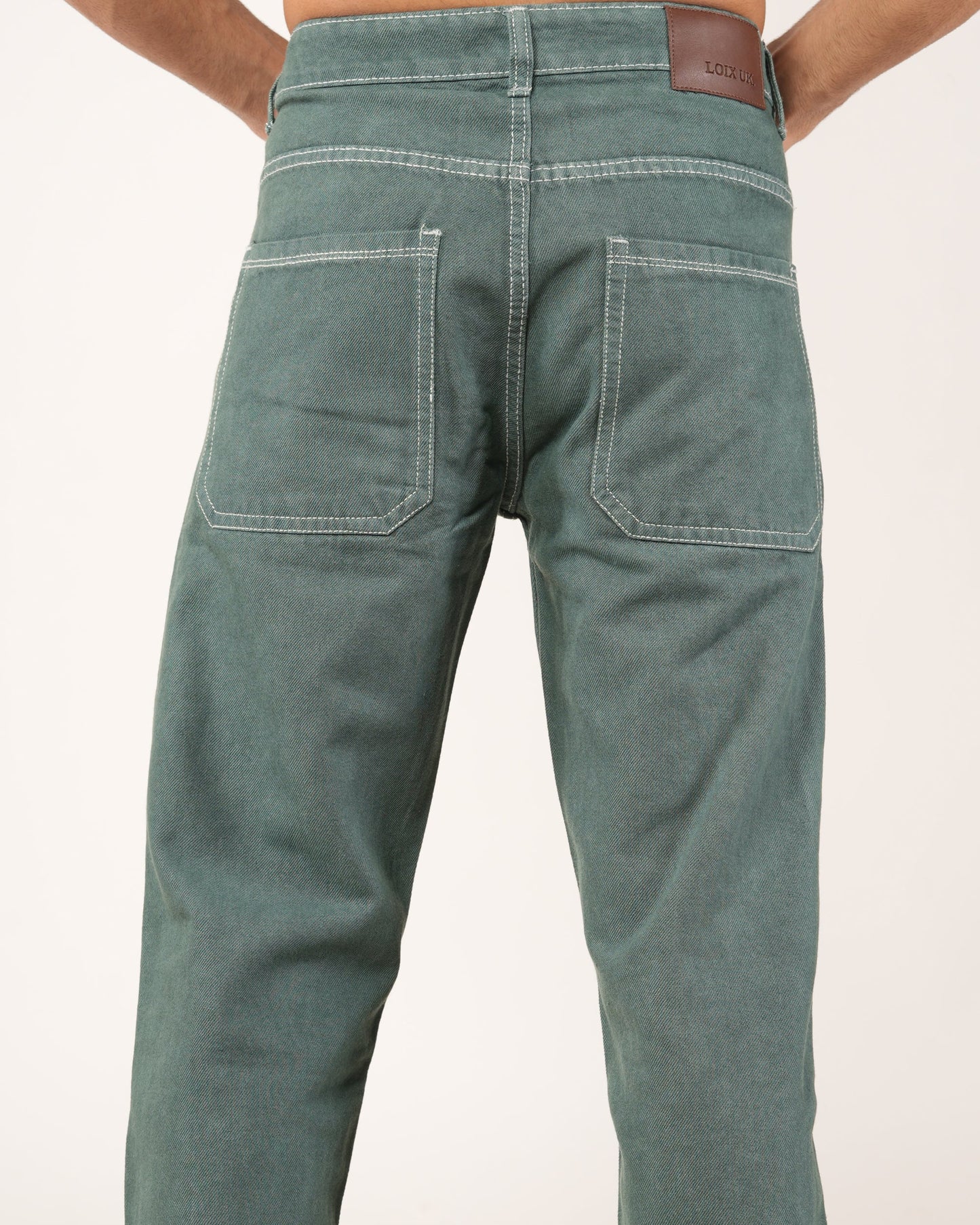 Rear view of a person wearing green denim jeans with a brown leather brand patch on the waistband, set against a plain white background.