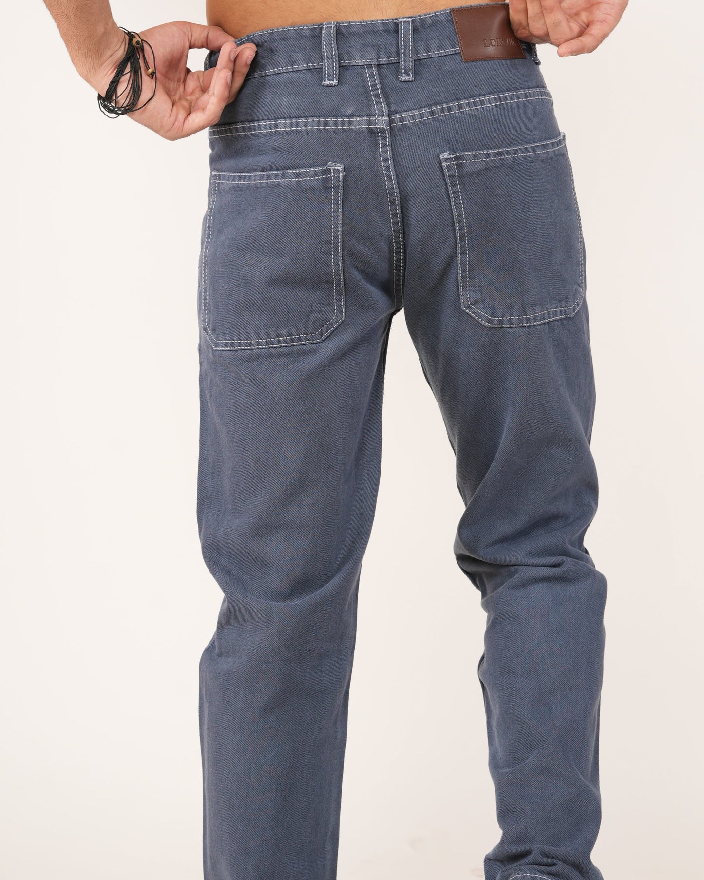 Rear view of a person wearing slate blue straight-fit jeans, showing the back pockets, waistband, and leather patch detail.