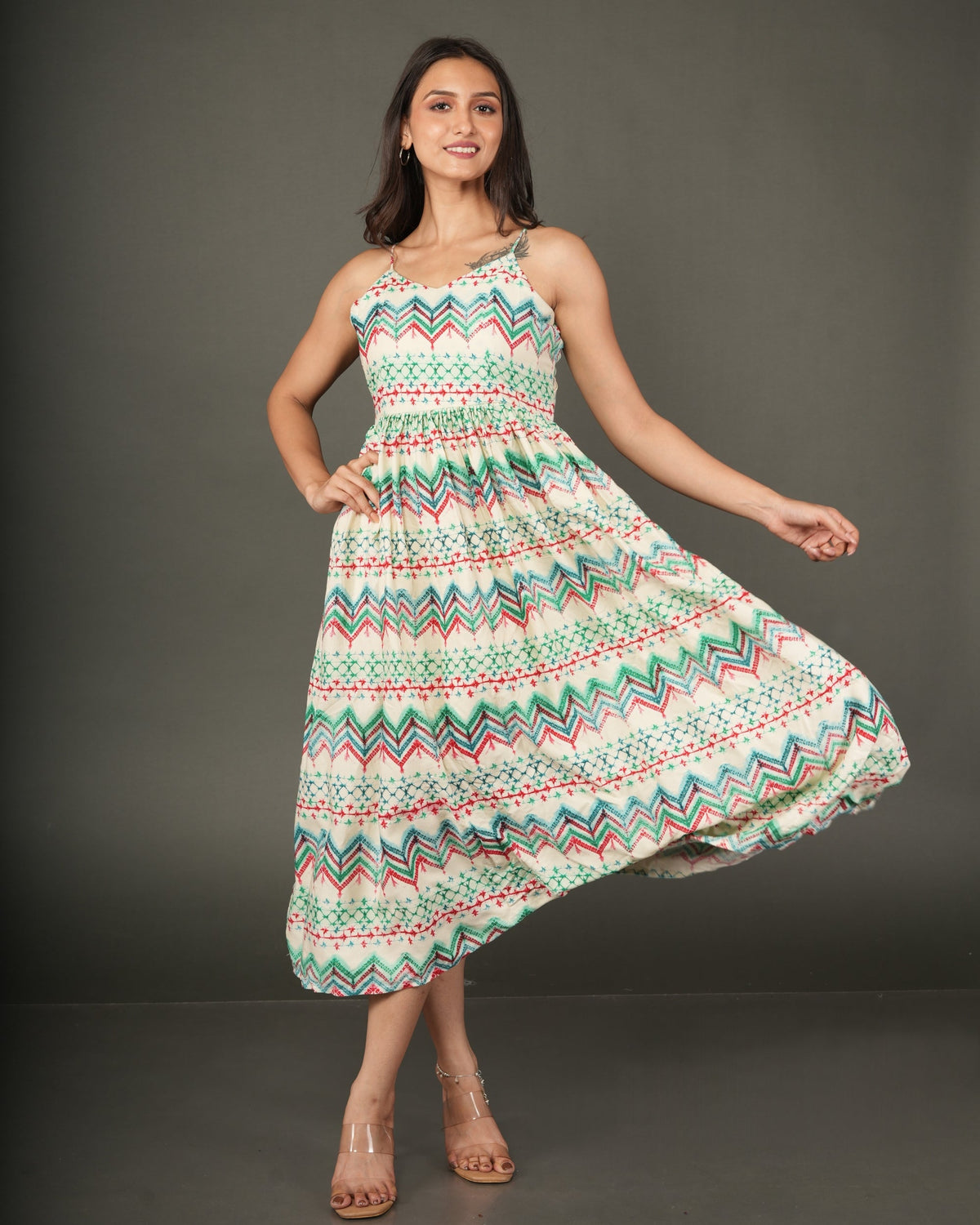 A woman modeling a sleeveless midi dress with a colorful geometric zigzag pattern in green, orange, and white